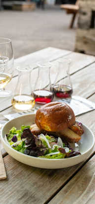 A meal consisting of a sandwich and salad is served on a table with two glasses of wine.