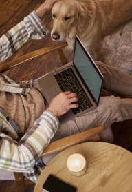 a person sitting on a chair with a dog using a laptop at The Mark, San Antonio, TX 78230
