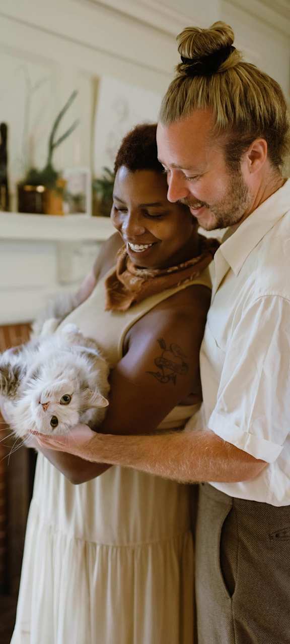 A man and woman holding a cat in a living room.
