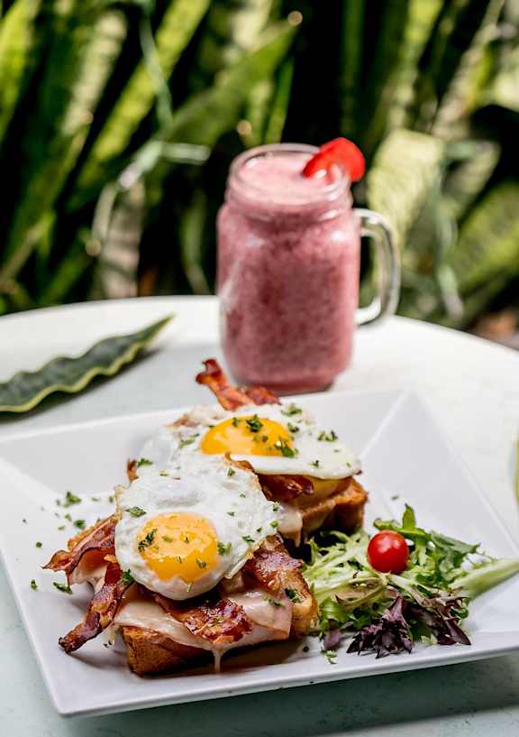 A breakfast plate with eggs, bacon, and a side salad next to a smoothie.