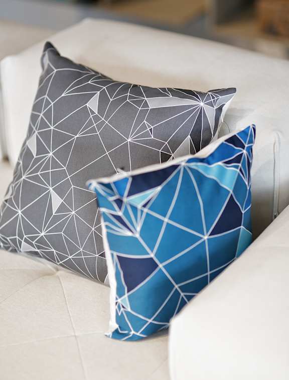 Three pillows with geometric patterns are on a white couch.