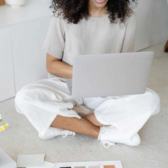 A person is sitting on the floor with a laptop, surrounded by color swatches and design samples.