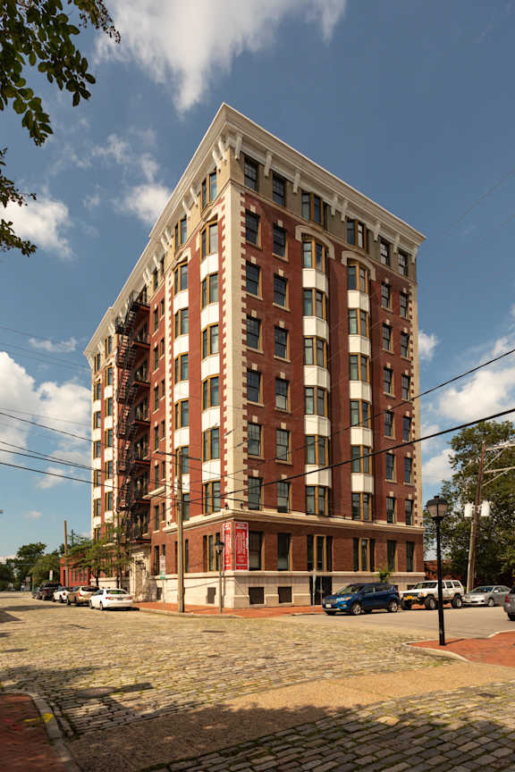 A tall red brick building with many windows and a parking lot in front.