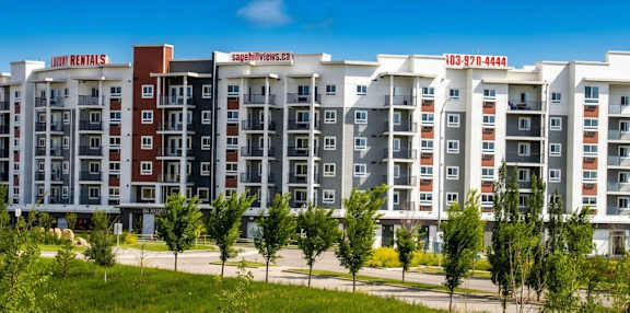 A large, modern apartment building with a red and white sign on the top.