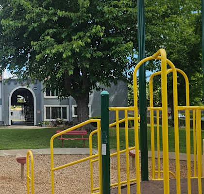 A playground with a yellow slide in front of a grey building.