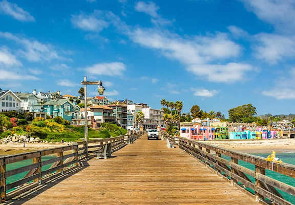 A wooden pier leads to a beach with colorful buildings on the shore.