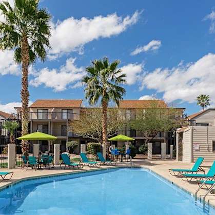 A pool surrounded by lounge chairs and palm trees.