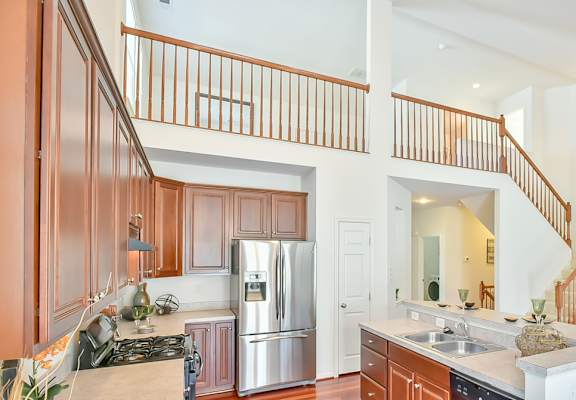 A photo of a bright kitchen with wood cabinets and an open second floor above.