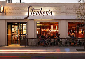 a restaurant on the side of a street with people sitting at tables