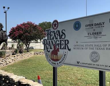 A sign for the Texas Ranger Museum is displayed in front of a statue of a ranger on a horse.