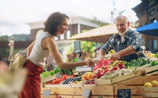 A woman is buying vegetables from a man at a market.