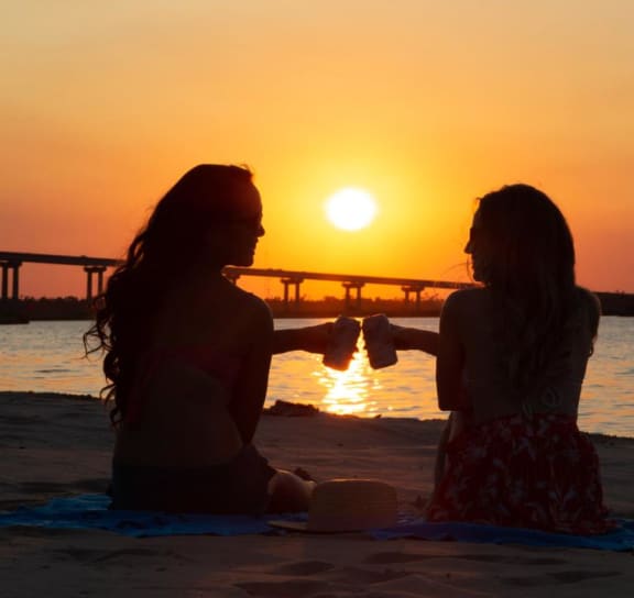 a couple of women sitting on a beach at sunset