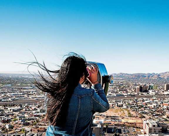 A woman is looking through binoculars at a cityscape.