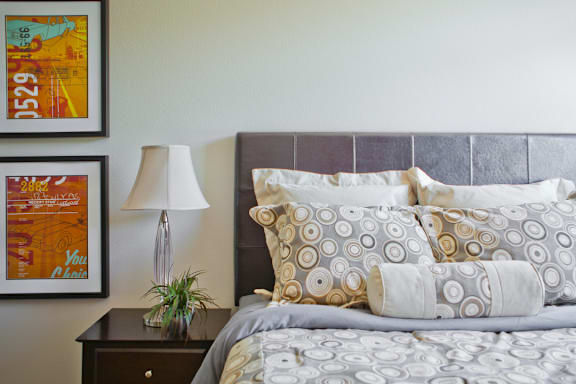 A bed with a grey headboard and a grey comforter with a pillow on it.