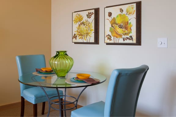 A glass table with a green vase and two chairs.