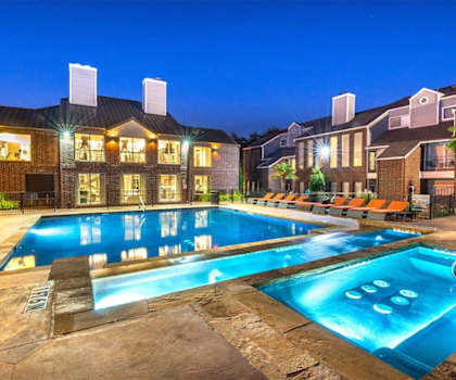 The turquoise outdoor pool with pool chairs, tables, and chairs with the apartments in the background at Lakewood on the Trail. 