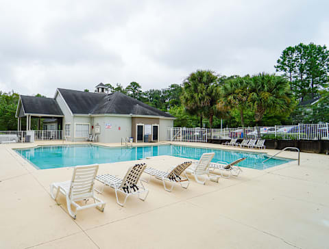a swimming pool with chaise lounge chairs and a club house in the background
