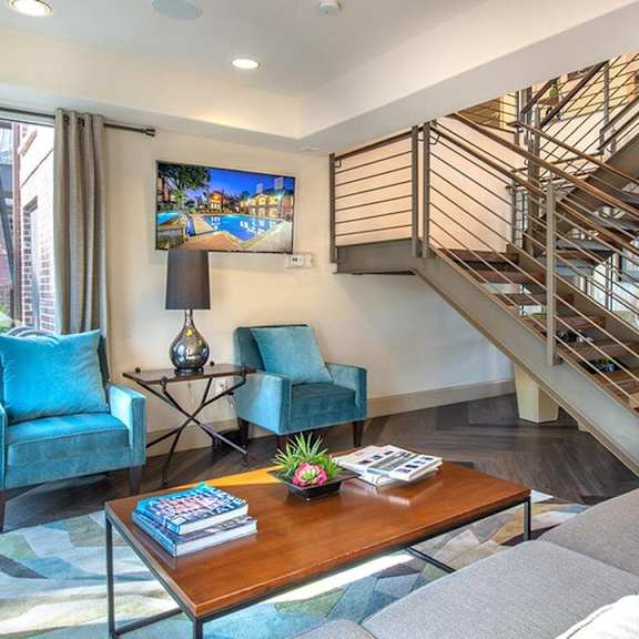 The downstairs community lounge with plush chairs, a couch, and large windows with natural lighting at Lakewood on the Trail. 