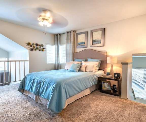 A bedroom with a queen-size bed, a dresser, decorations, window, and nightstands with stairs going downstairs at Lakewood on the Trail. 