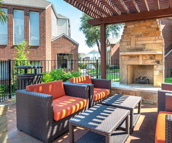 The outdoor resident lounge with a fireplace, decorations, orange plush chairs, and coffee tables at Lakewood on the Trail. 