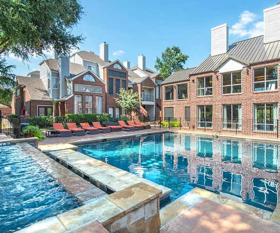 The turquoise outdoor pool with pool chairs, tables, and chairs with the apartments in the background at Lakewood on the Trail.