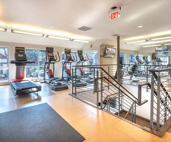 A gym with cardio machines, windows, TVs, and weights at Lakewood on the Trail. 