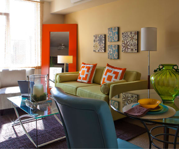 A living room with a glass table and a green vase on it.