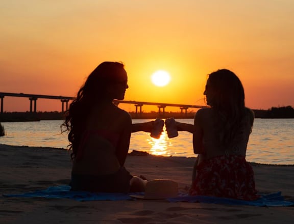 a couple of women sitting on a beach at sunset