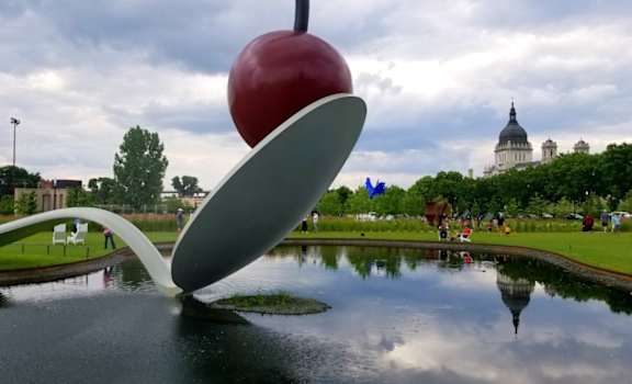 A large red apple is balanced on top of a white, curved structure in a park.