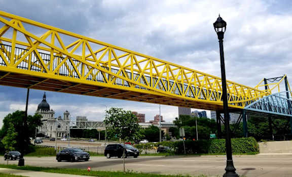 A yellow bridge spans over a road with cars and a lamp post.