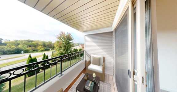 A balcony with a white chair and a table with a bottle on it.