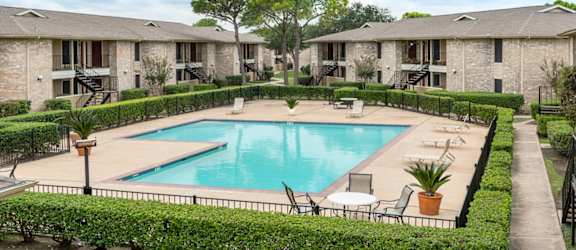 a swimming pool with chairs around it in front of apartments