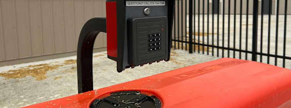A red car is parked next to a black gate with a parking meter attached to it.