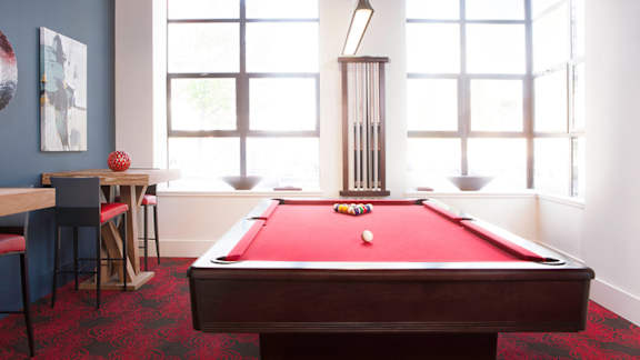 A pool table with a red cloth and white balls is in the center of the room at Skye at Belltown Apartments in Washington 98121