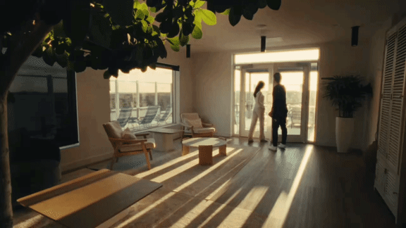 A man and woman are standing in a sunlit living room.