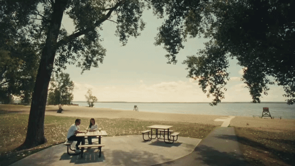 Two people sitting at a picnic table by the water.