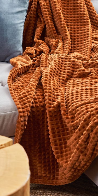 a couch with a blanket on it and a coffee cup on a table