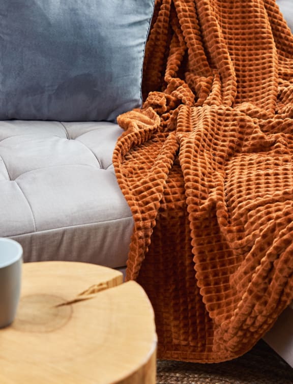 a couch with a blanket on it and a coffee cup on a table