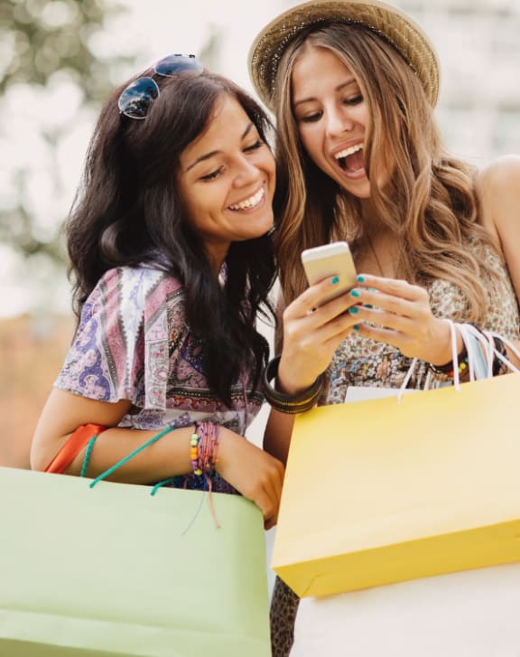 two women looking at a cell phone while holding shopping bags