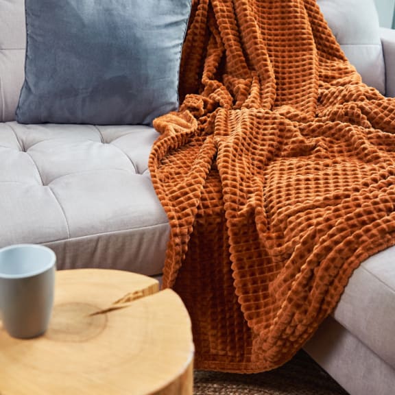 a couch with a blanket on it and a coffee cup on a table