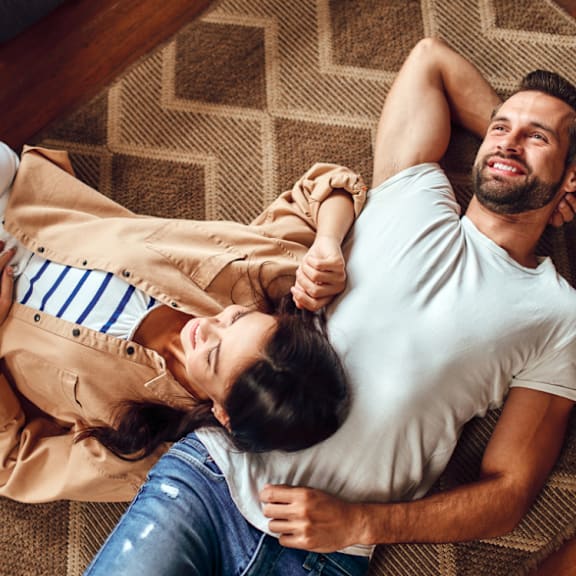 A man and woman are lying on a rug, embracing each other.
