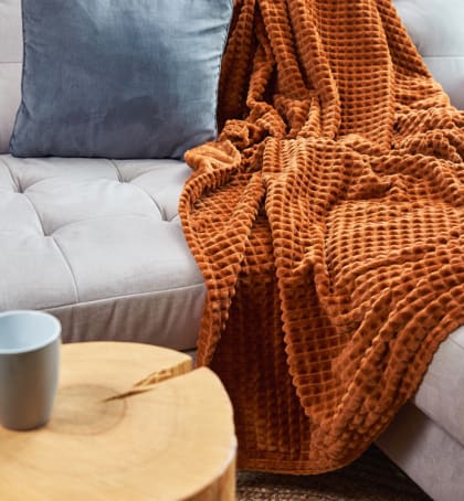 a couch with a blanket on it and a coffee cup on a table