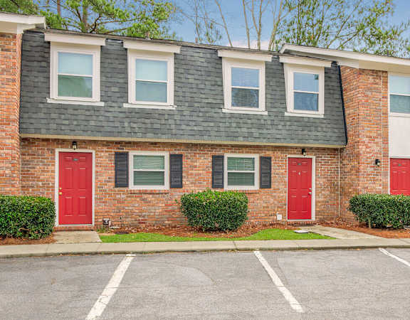 a brick apartment building with red doors and a parking lot at Savan Pointe Townhomes East and West, Savannah