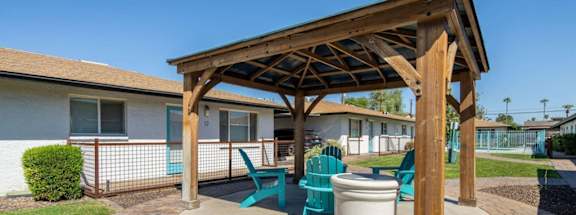 a patio with a wooden pavilion with chairs and a trash can