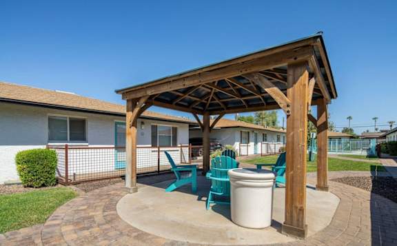 a patio with a wooden pavilion with chairs and a trash can