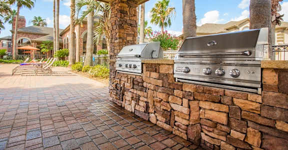 a barbecue grill on a stone wall in a backyard with palm trees