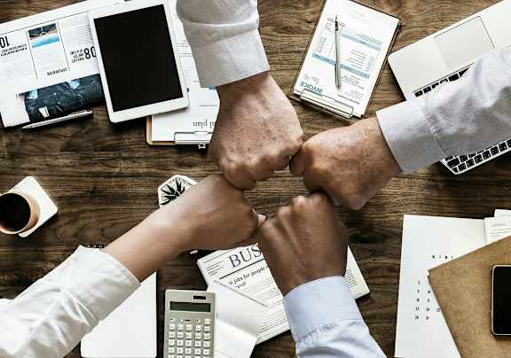 Two people fist bumping over a desk with various office supplies.