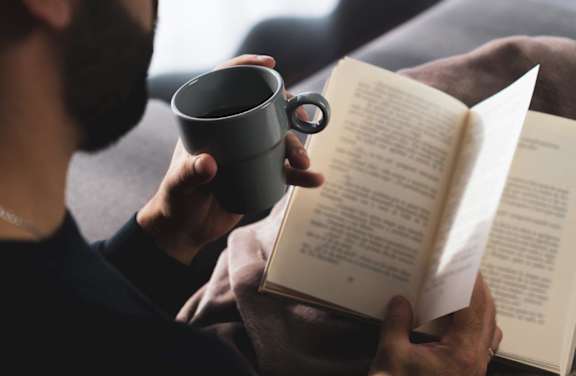 Man Holding Cup of Coffee and Reading Book