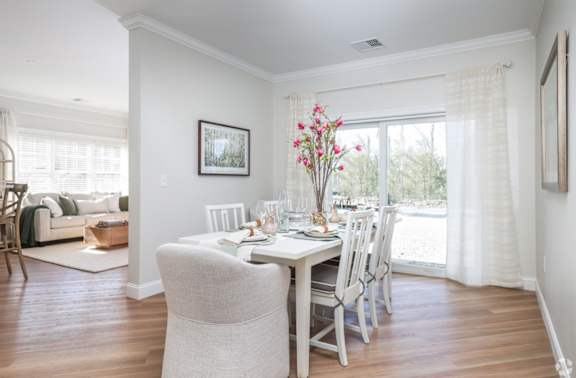 A dining room with a table set for two and a couch in the background.