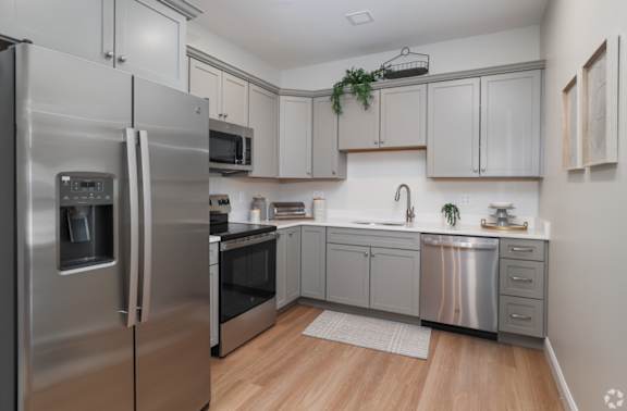 A modern kitchen with a stainless steel refrigerator and wooden flooring.